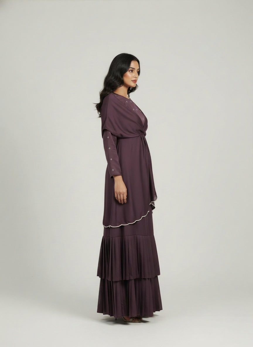 Woman wearing a long, dark purple dress with ruffled layers on a white background