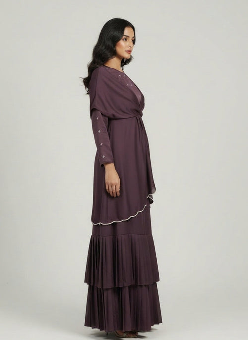 Woman wearing a long, dark purple dress with ruffled layers on a white background
