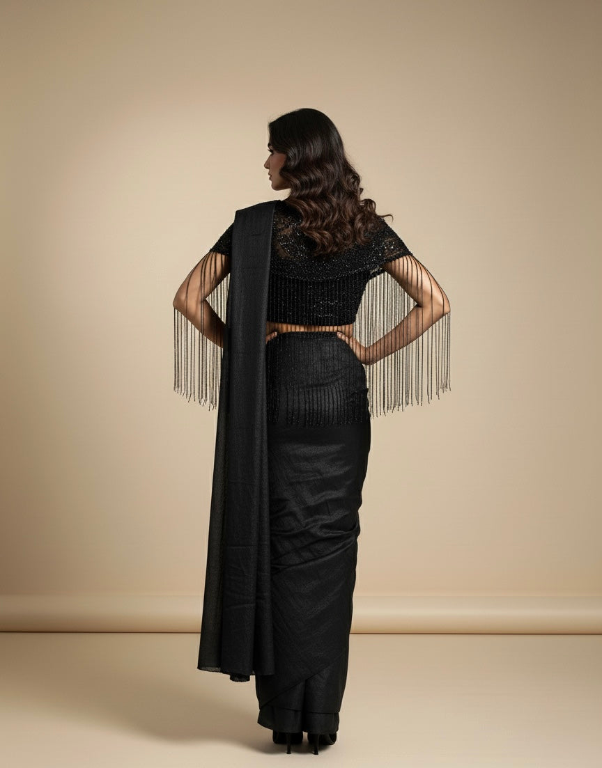 Woman wearing a black saree with a matching blouse against a beige background