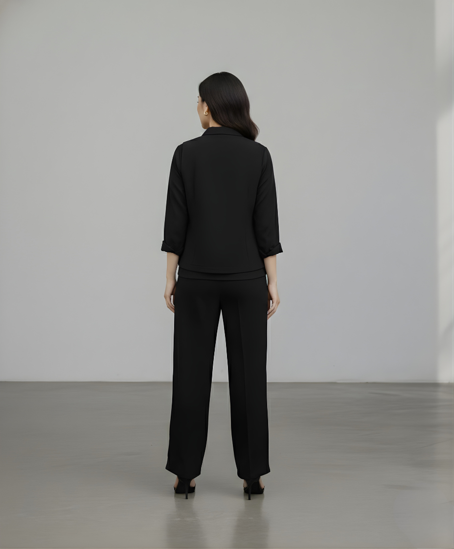 Person wearing a black suit standing against a plain white wall.