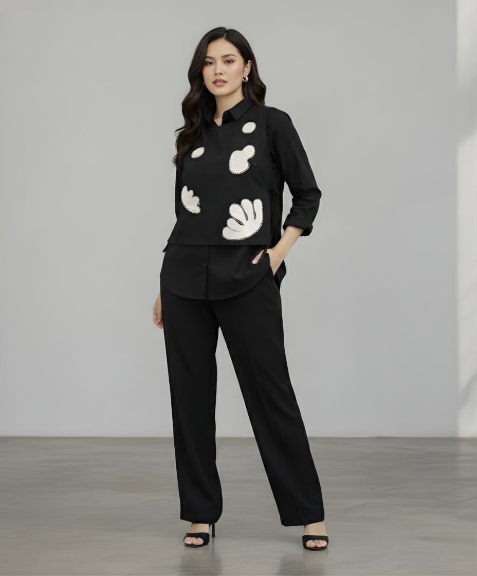 Woman wearing a black blouse with white patterns and black pants against a plain background