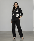 Woman wearing a black blouse with white patterns and black pants against a plain background