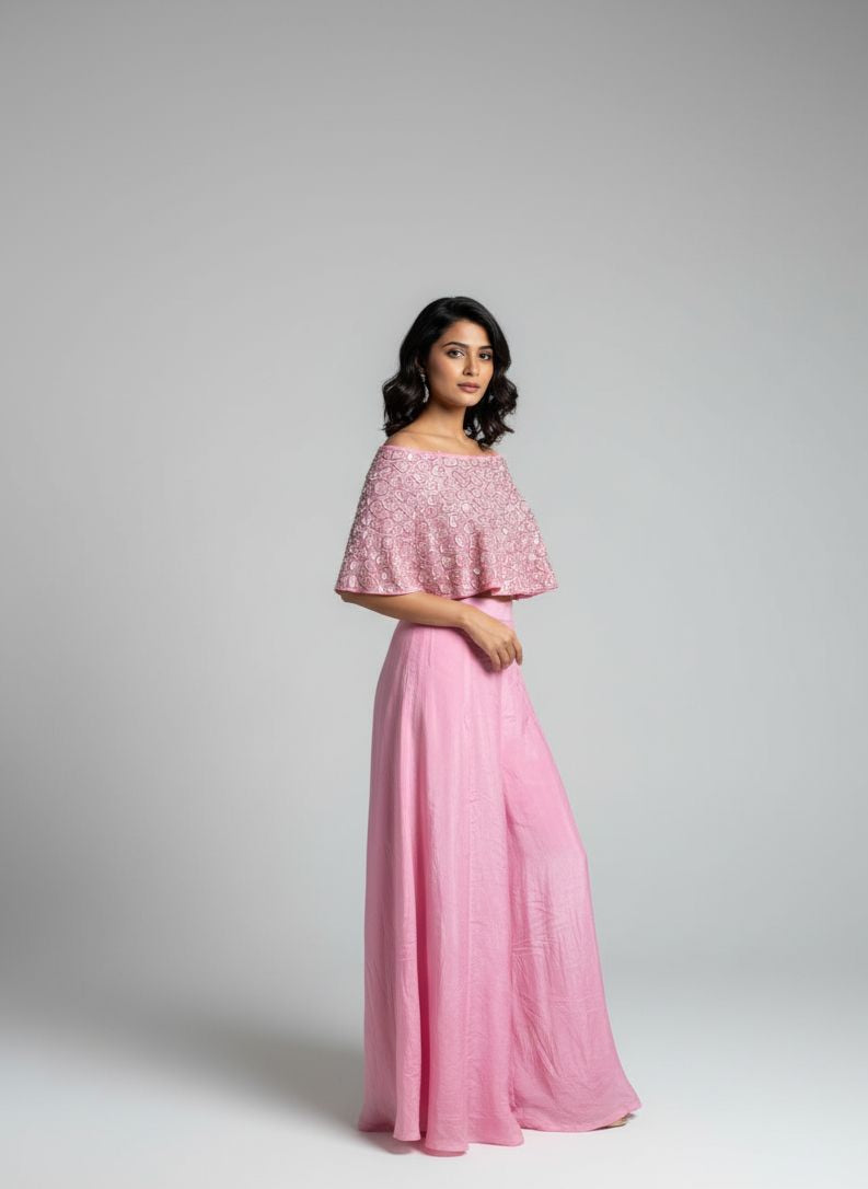 Woman wearing a pink outfit with a cape-like top on a gray background