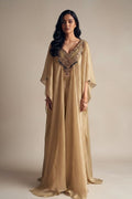 Woman wearing a long, beige dress with intricate detailing on a plain background
