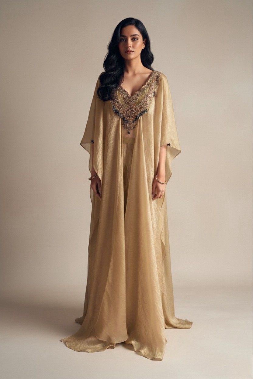 Woman wearing a long, beige dress with intricate detailing on a plain background