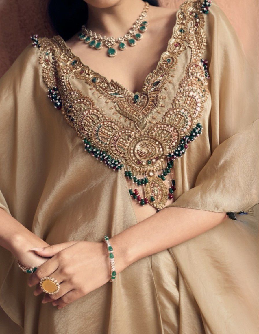 Close-up of a person wearing intricate jewelry and a beige outfit with detailed embroidery.