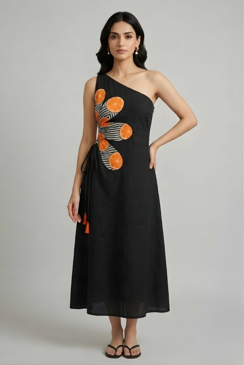 Woman wearing a black one-shoulder cotton midi dress with orange citrus print detailing and wrap tie waist, minimal studio background, modern summer fashion