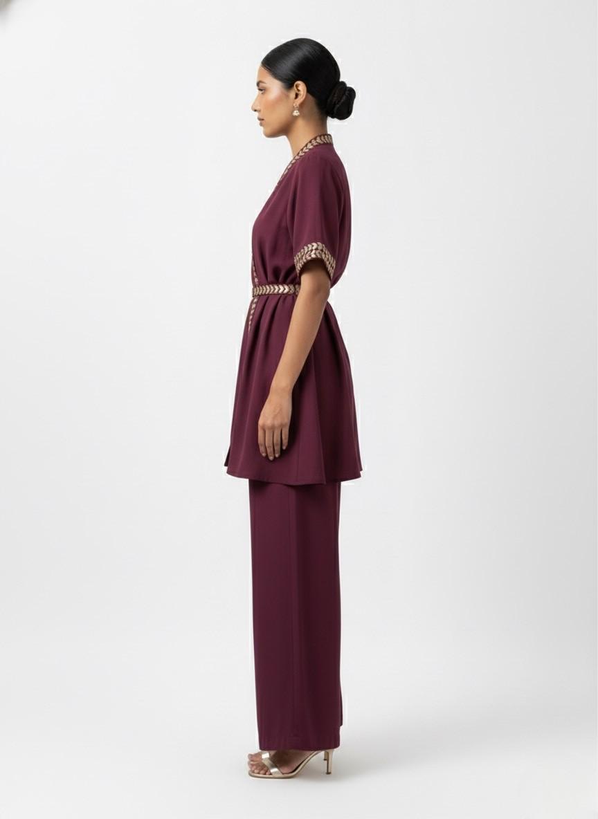 Woman wearing a dark maroon outfit with gold handwork on a white background