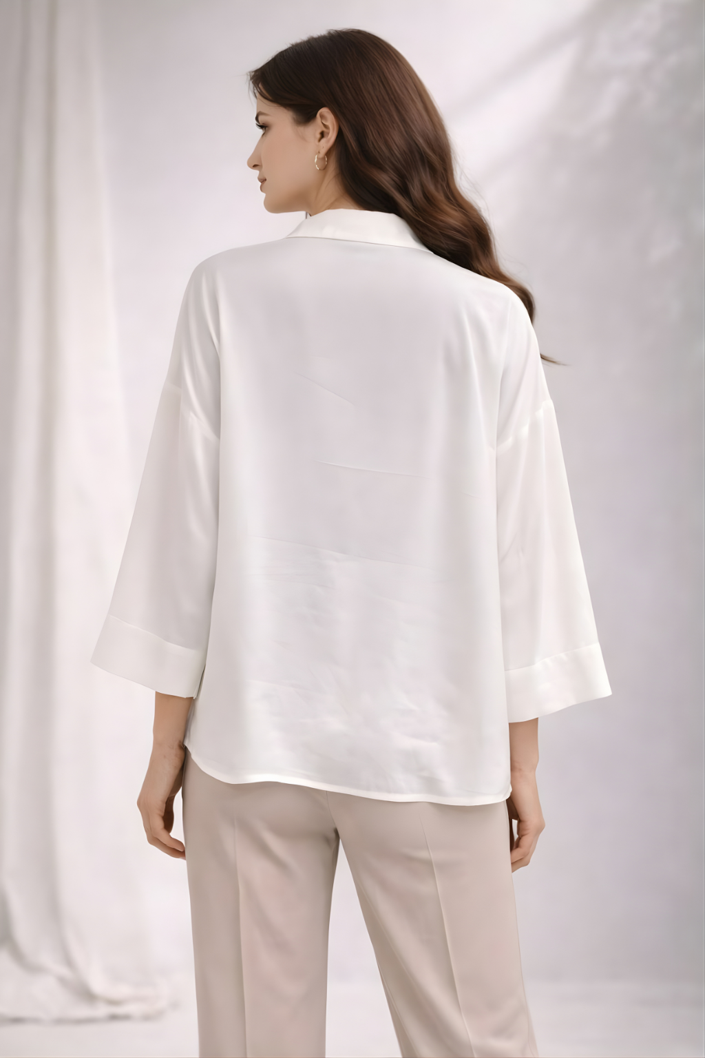 Woman wearing a white shirt and beige pants against a plain background