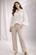 Woman wearing a white blouse with yellow patterns and beige pants on a plain background