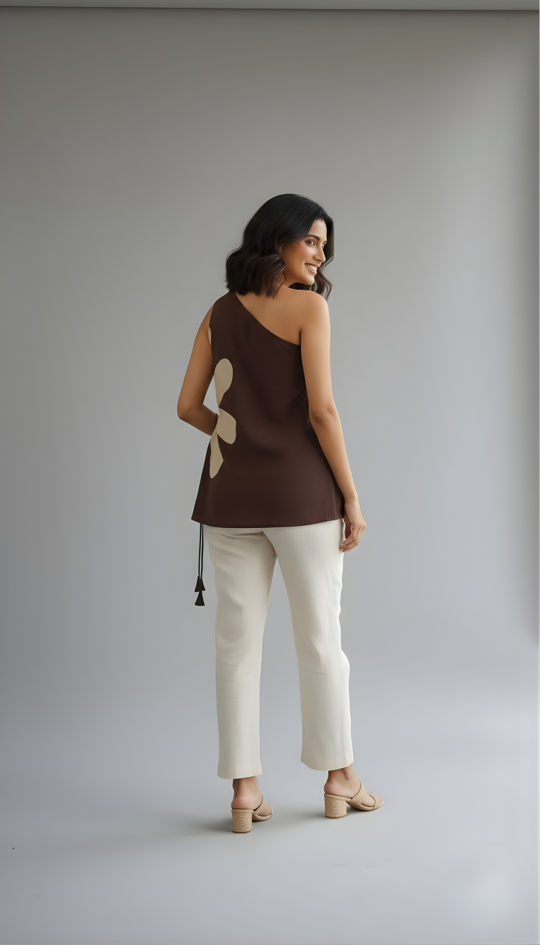 Sleeveless one-shoulder brown designer top with artistic patch detail shown on a model in a clean neutral background.