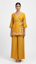 Woman wearing a mustard yellow outfit with floral embroidery on a white background