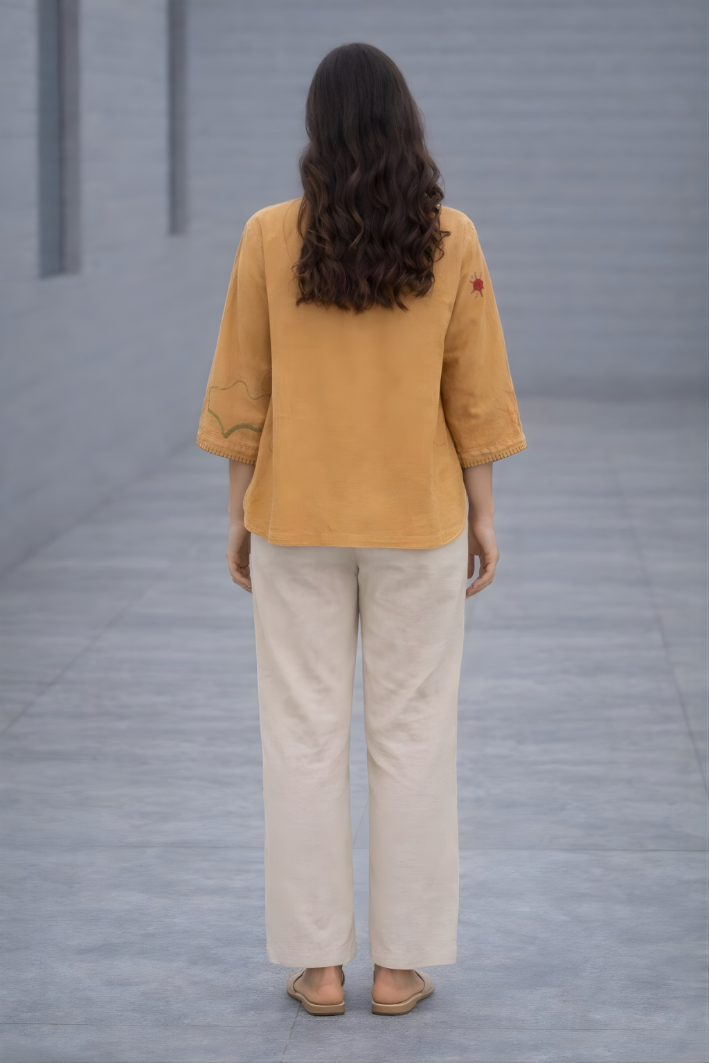 Person wearing a mustard yellow jacket and beige pants standing in a gray room.