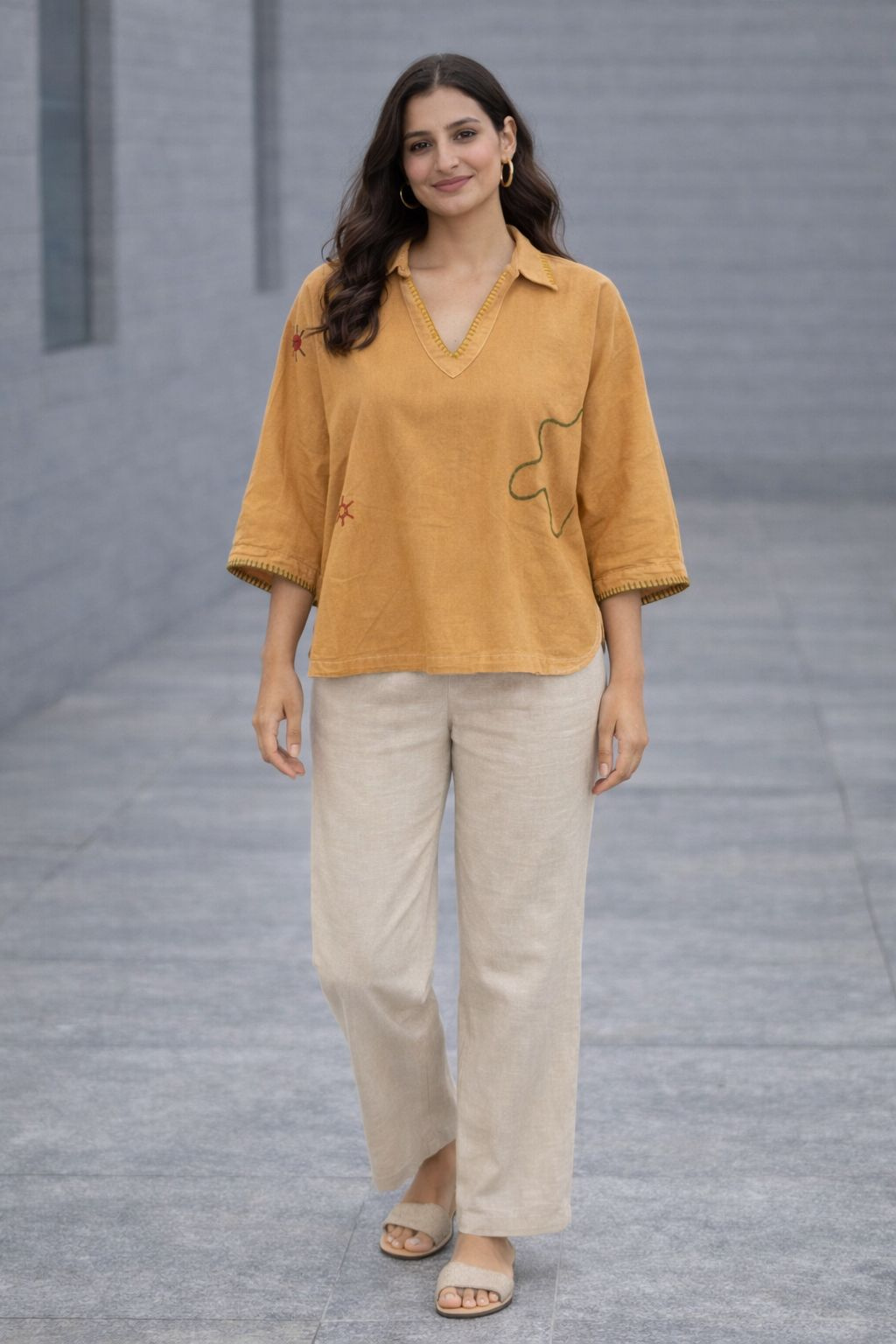 Woman wearing a mustard yellow top and beige pants standing on a gray pavement.