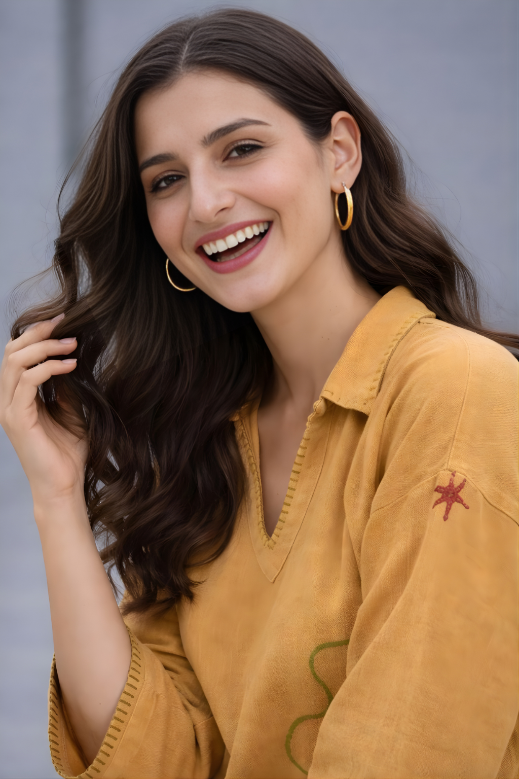 Woman wearing a mustard yellow top with a subtle smile against a neutral background