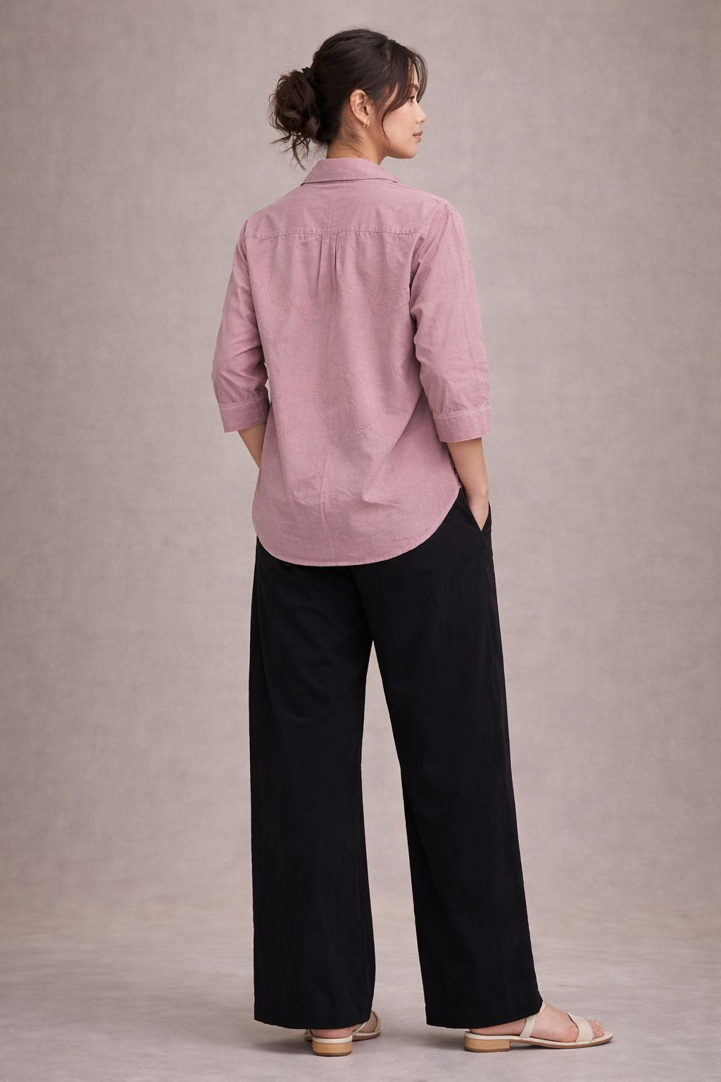 Woman wearing a pink shirt and black pants against a plain background