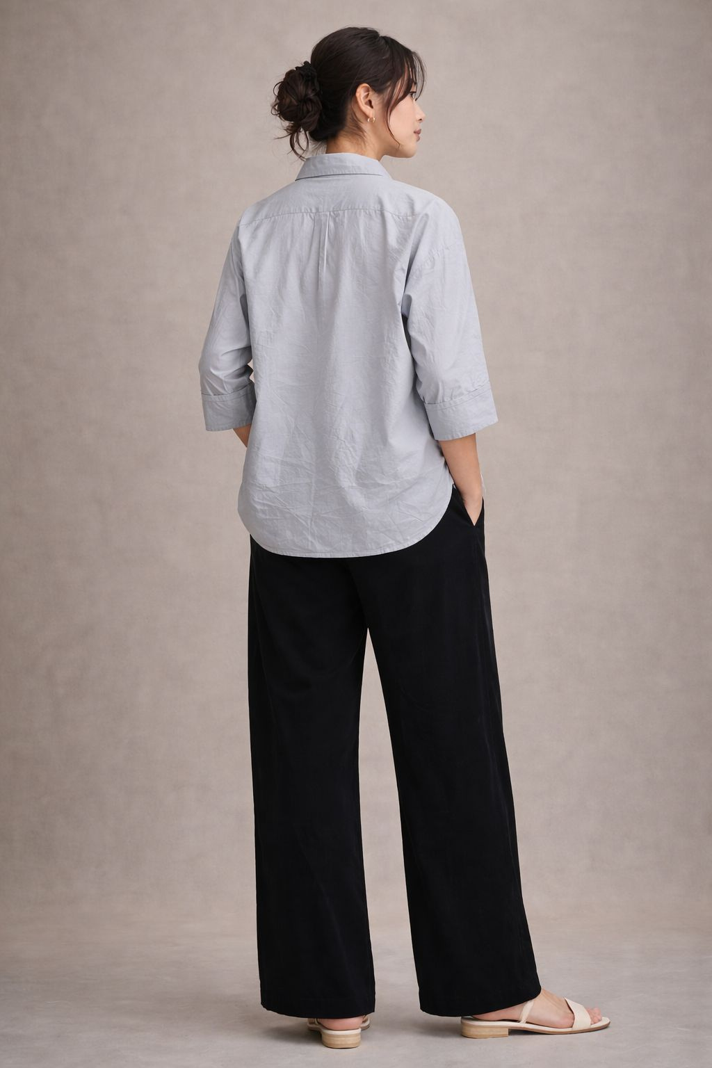 Woman wearing a light gray shirt and black pants against a beige background