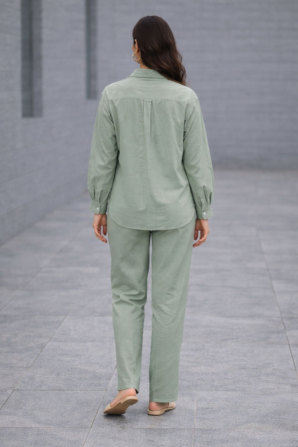 Person wearing a green outfit walking on a gray pavement.