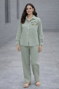 Woman wearing a light green shirt and pants set with floral embroidery on a gray pavement background