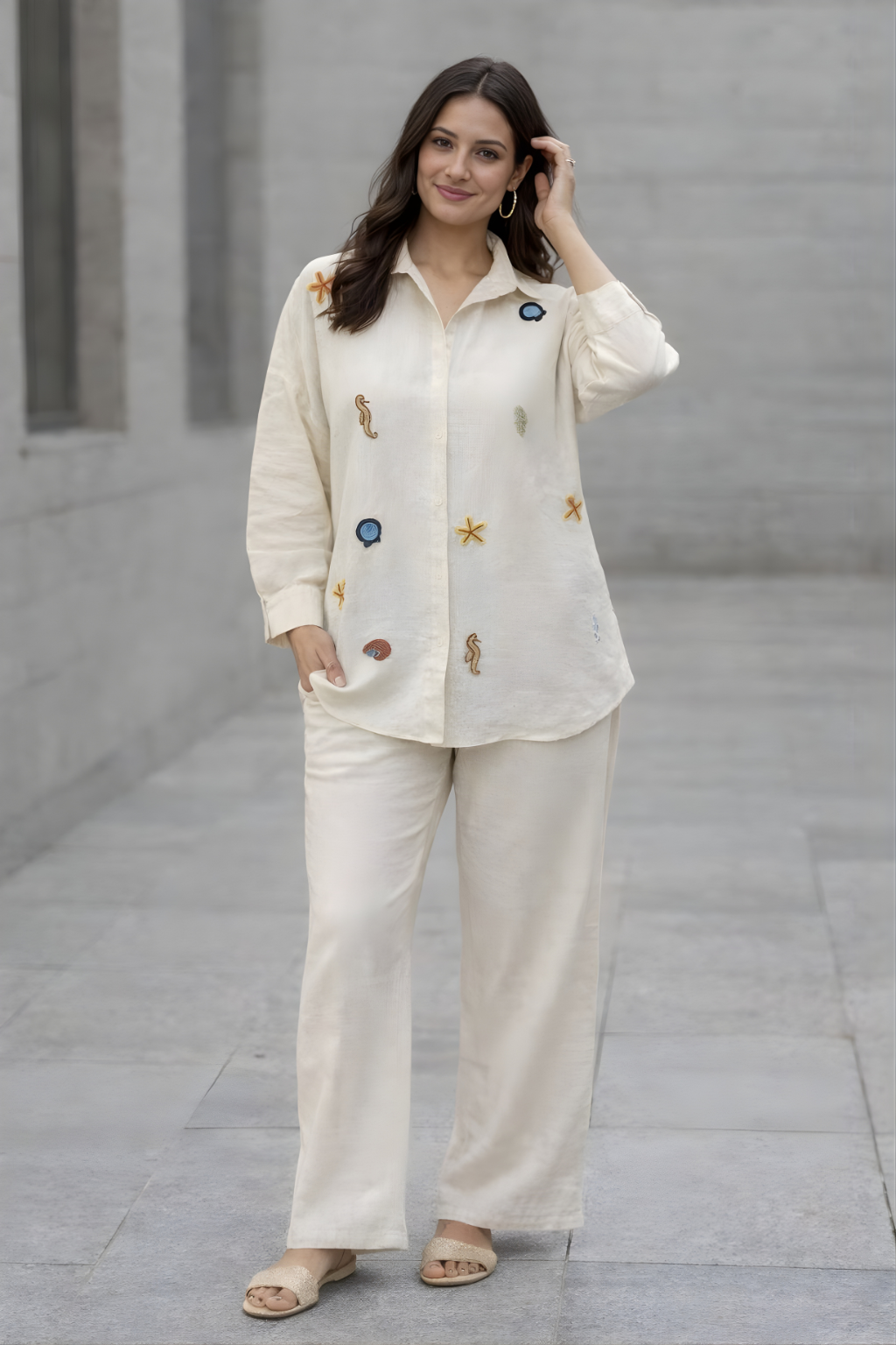 Woman wearing a cream-colored outfit with decorative buttons against a gray wall.