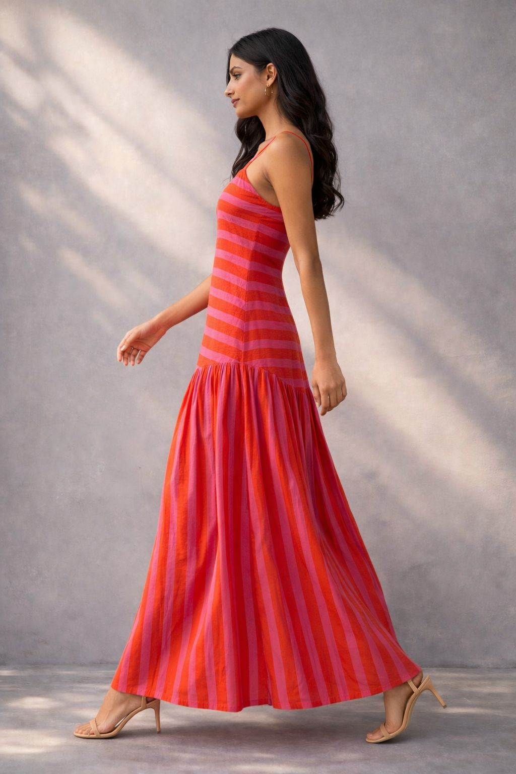 Woman wearing a pink and orange striped cotton maxi dress with spaghetti straps and a flared hem