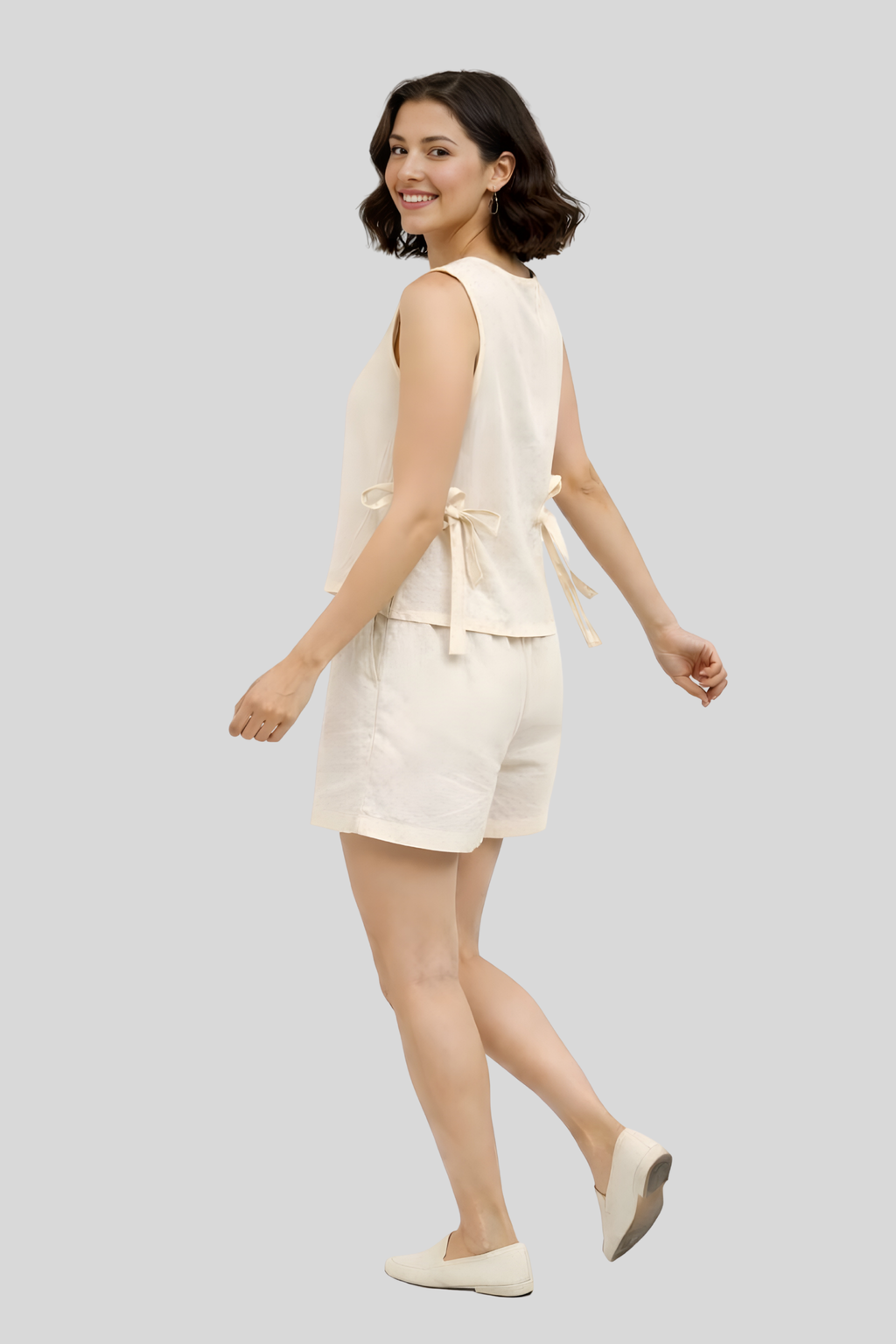 Woman wearing a cream-colored outfit with a top and shorts on a light gray background