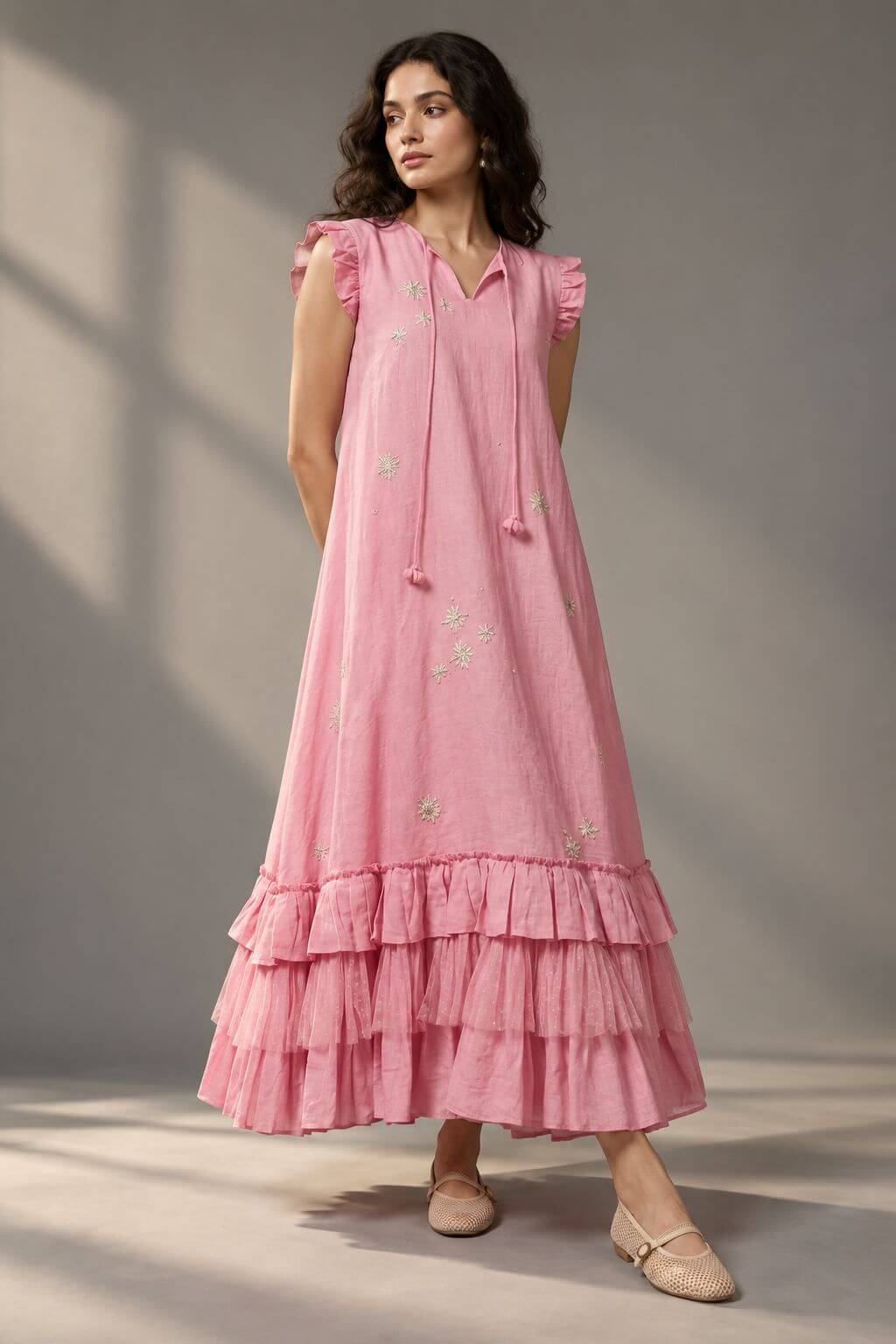  Woman wearing a blush pink tiered midi dress with floral embellishments and ruffled sleeves