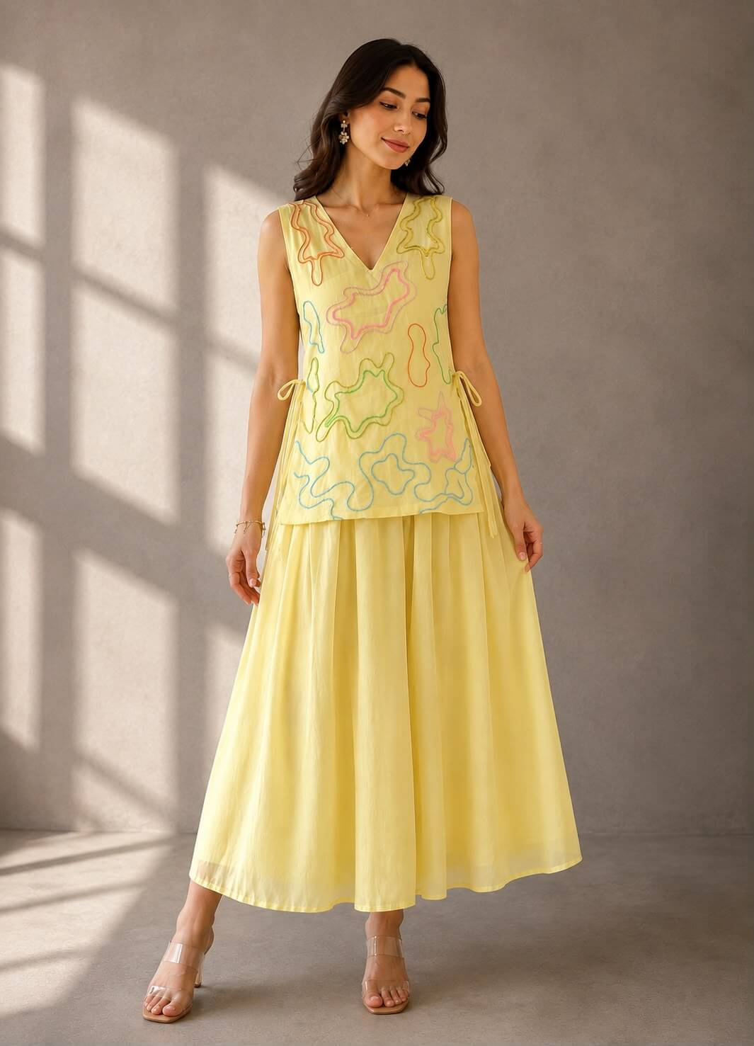 Woman wearing a butter yellow cotton umbrella dress paired with a detachable embellished vest featuring colourful abstract detailing.