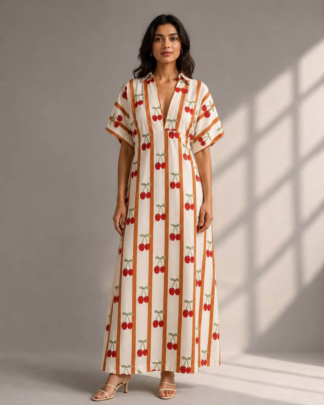 Woman wearing a cherry print striped cotton maxi dress with V-neck and kimono sleeves.