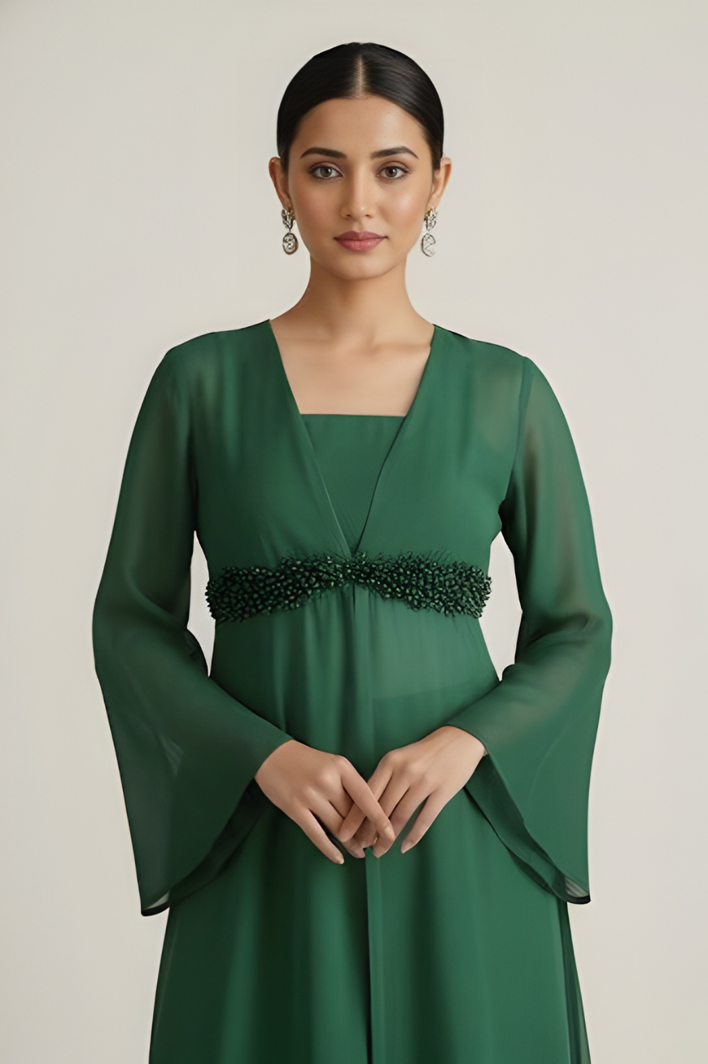Woman wearing a green dress with a beaded belt against a plain background
