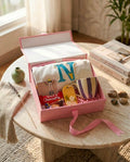 Gehru Bliss Box featuring a customized alphabet T-shirt, handcrafted Rakhi, purple striped ceramic mug, floral fragrance bar, Choco Pie, and premium pink gift box.