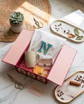 Gehru Serenity Box featuring a customized alphabet T-shirt, handcrafted Rakhi, cream ceramic mug, floral fragrance bar, and premium gift box