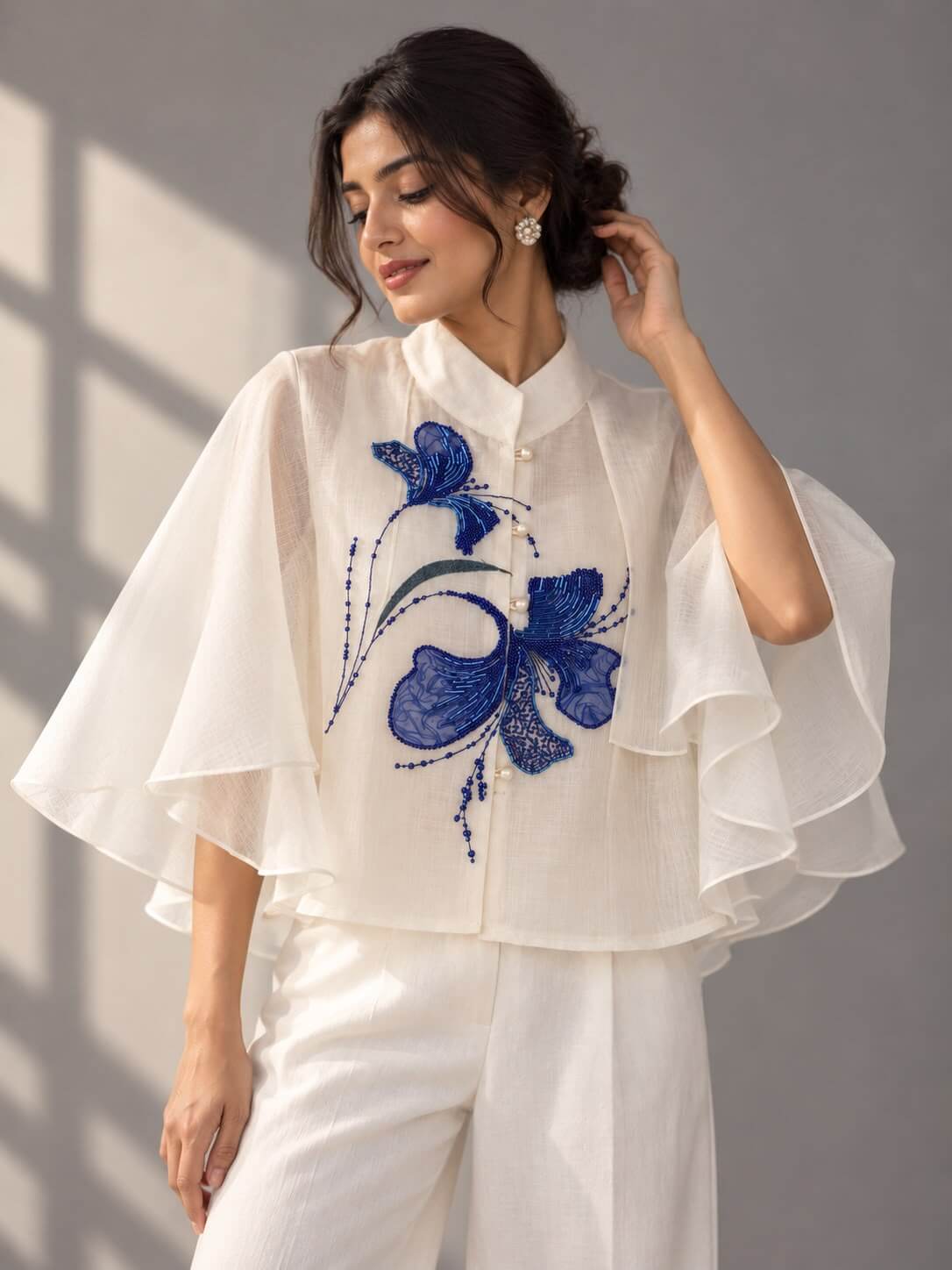 Front view of ivory cotton top with blue tubelight embellishment and layered ruffle sleeves