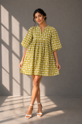 Indian model wearing olive check babydoll mini dress with puff sleeves in grey studio background with sunlight