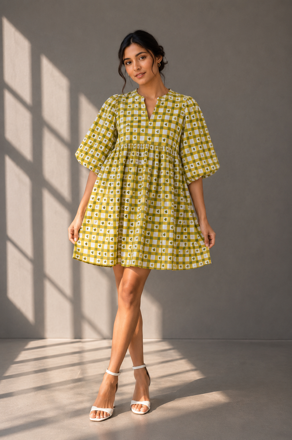 Indian model wearing olive check babydoll mini dress with puff sleeves in grey studio background with sunlight