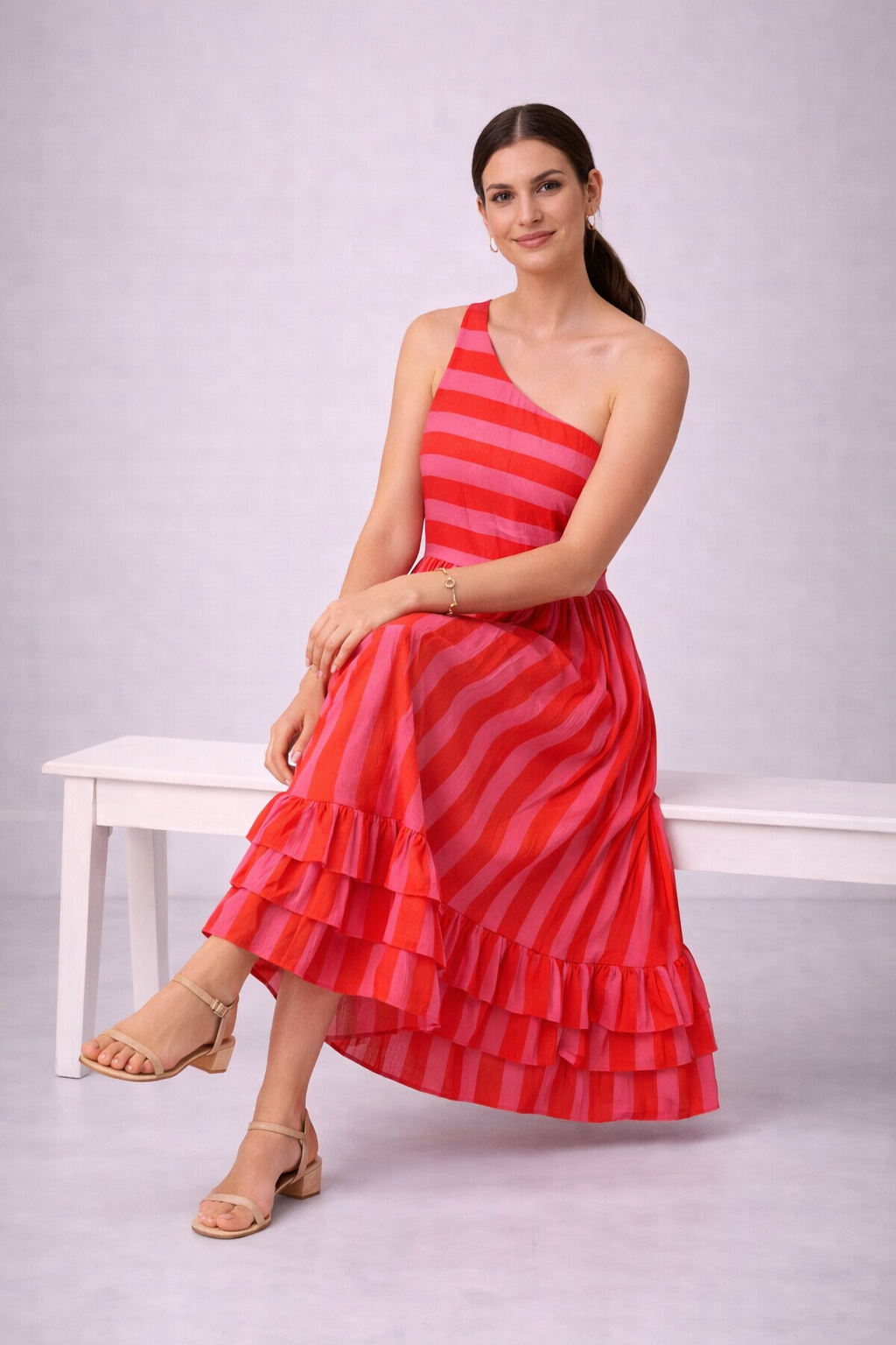 Woman wearing a orange and pink striped dress sitting on a white bench against a light gray background