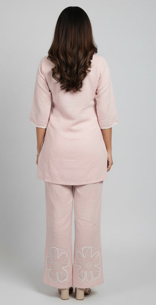 Woman wearing a light pink suit with embroidered pants on a white background