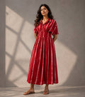 Woman wearing a handcrafted ruby red Shibori cotton midi dress with a shirt collar and smocked waist by Gehru Label.