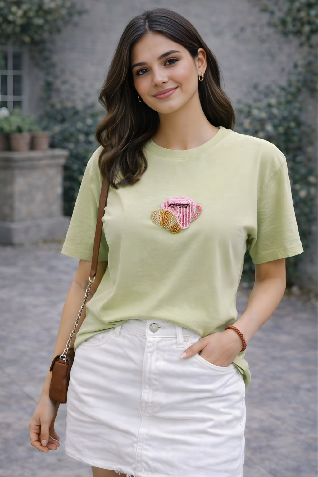 Woman wearing a sage green embellished T-shirt styled with a white skirt for a casual summer outfit.