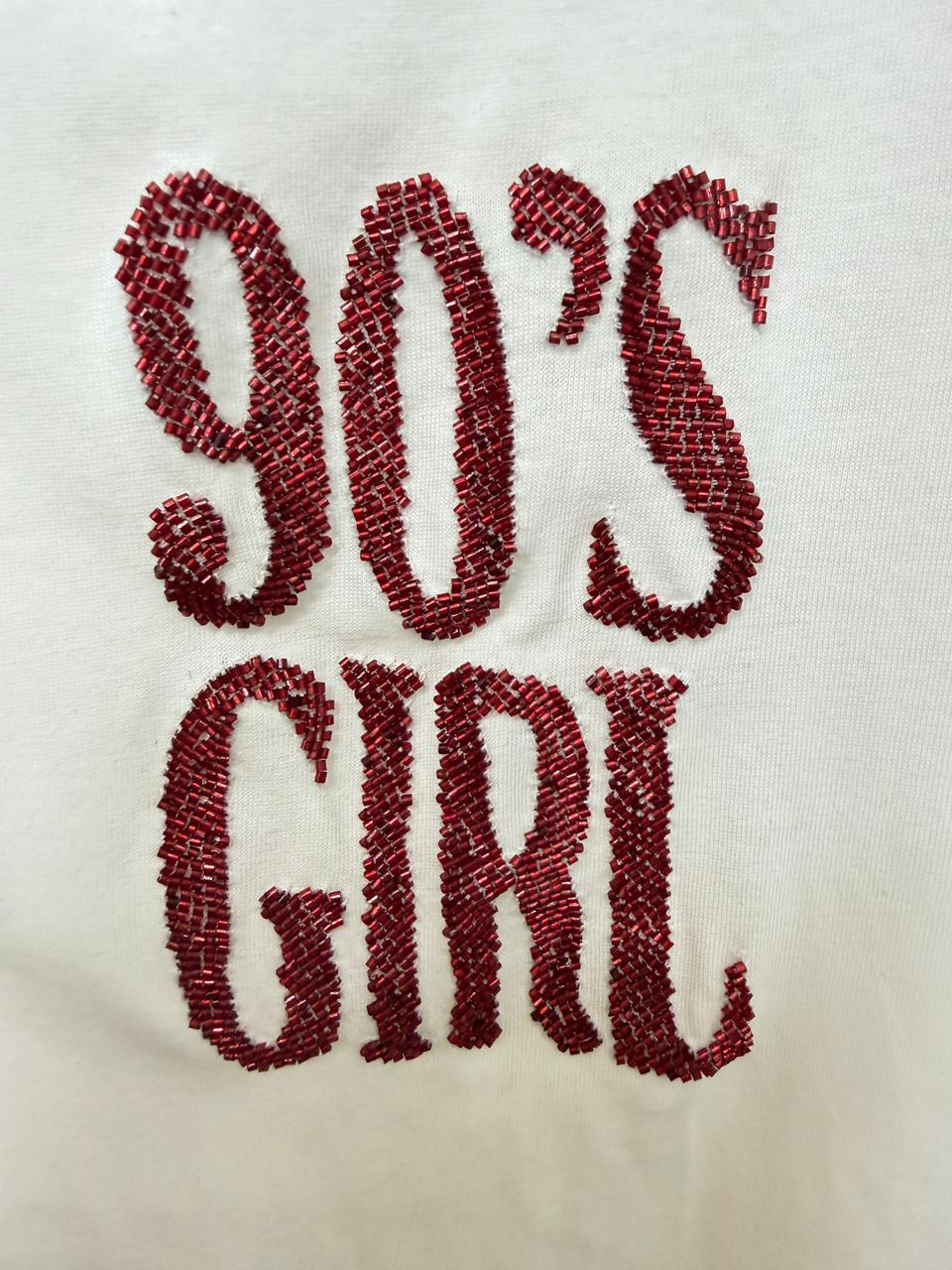 Woman wearing white 90s Girl graphic T-shirt with katdana embellishment.