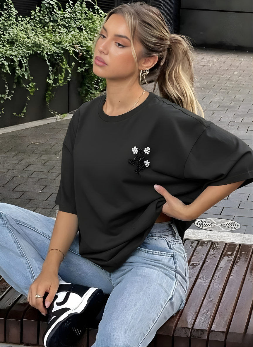 Woman wearing a black oversized t-shirt with floral designs and light blue jeans, sitting outdoors.